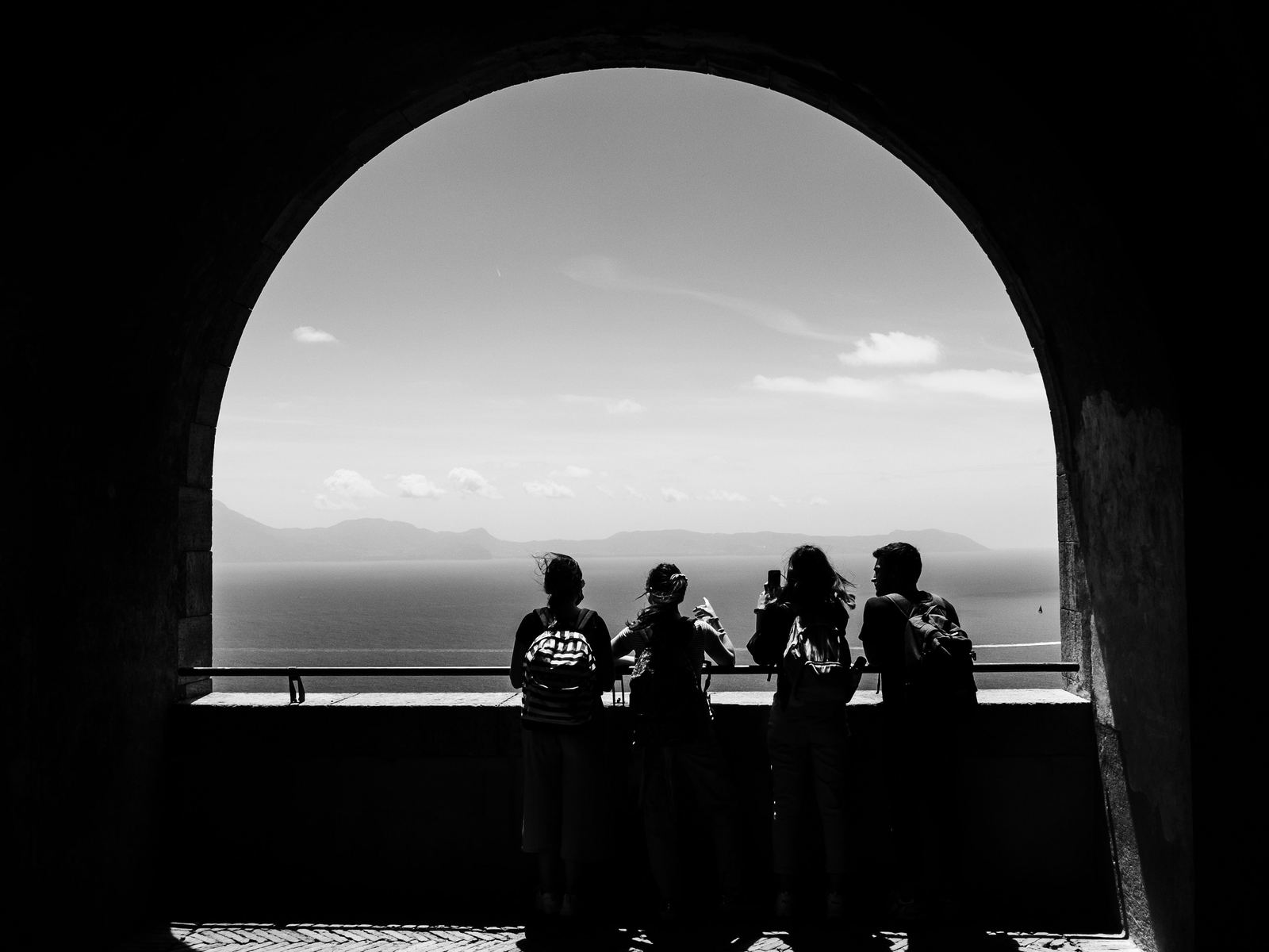 Four people silhouetted under a stone arch, looking out over the sea